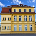 Gelbes Gebäude mit roten Dachziegeln und hohen Sprossenfenstern – Jobvermittlung durch Staff Eins.
